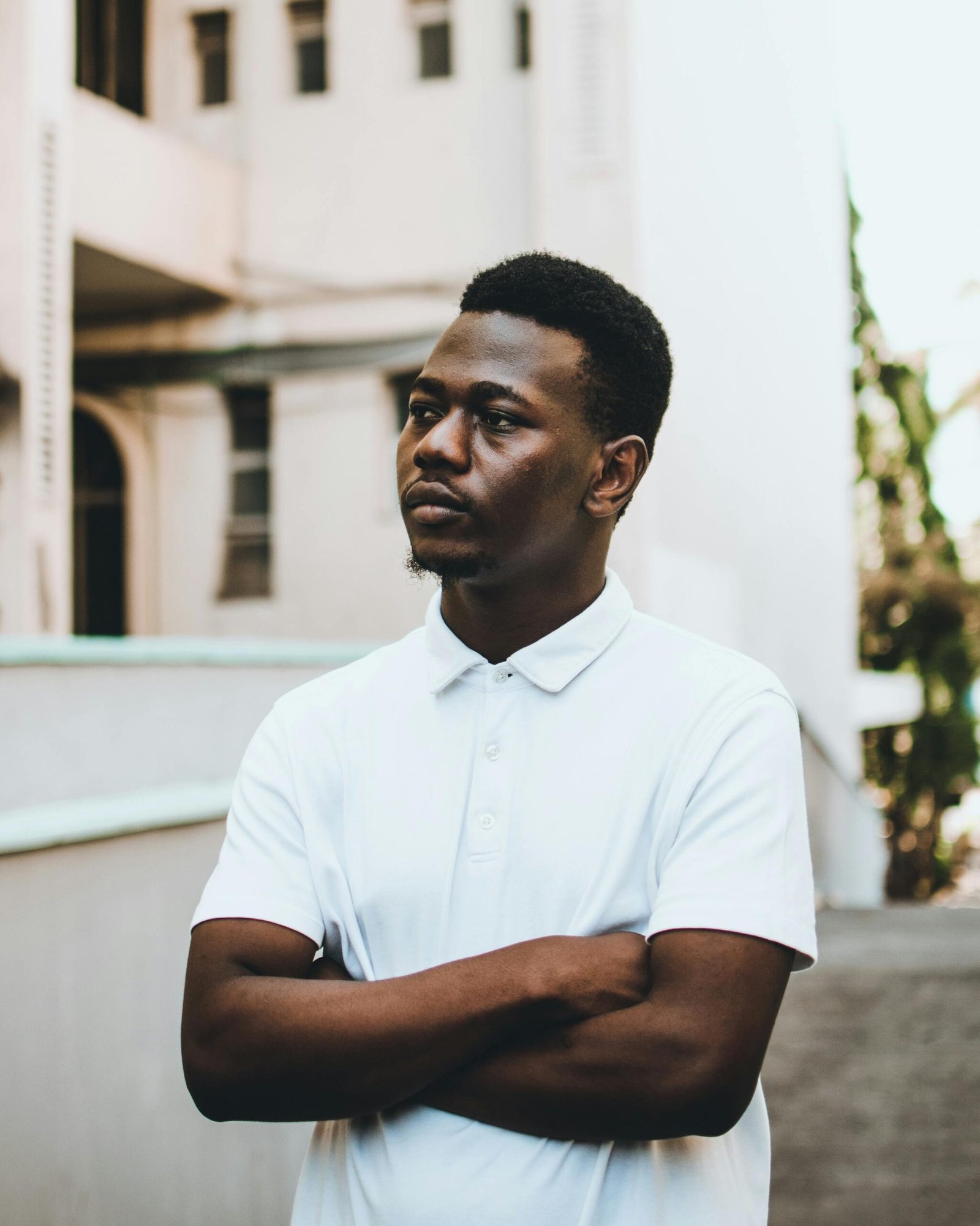 A young man poses seriously in a white polo shirt outdoors against a neutral background.
